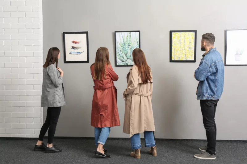 Four visitors standing in a row viewing framed works at a group show